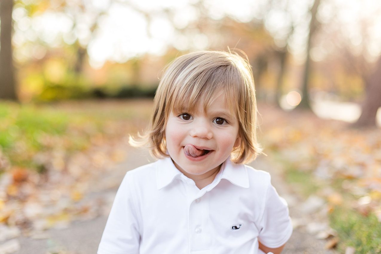 A little boy sticking his tongue out during his families fall portrait sessions at sherwood garden in baltimore