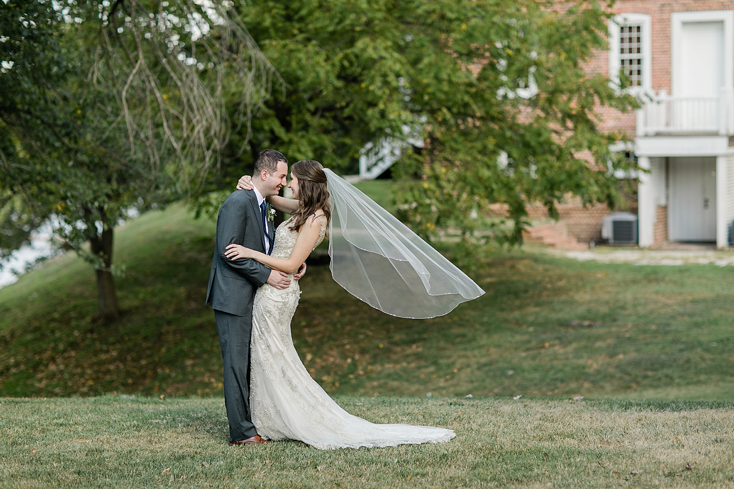 brunette woman in white dress embraces her groom on lawn by Baltimore wedding photographer