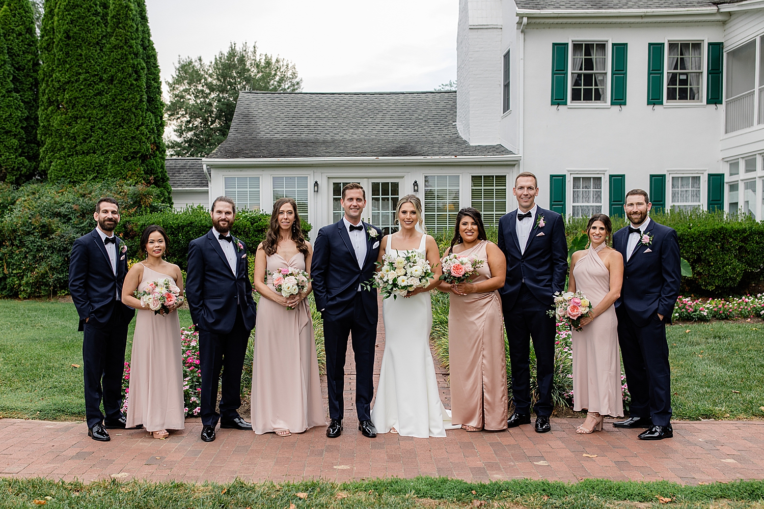 bridal party stands next to manor on brick path at Swan Harbor