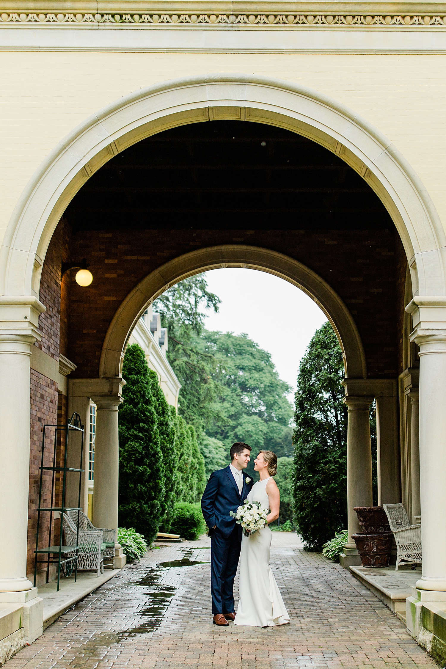 husband and wife stand under the oversized archway of venue by Baltimore wedding photographer