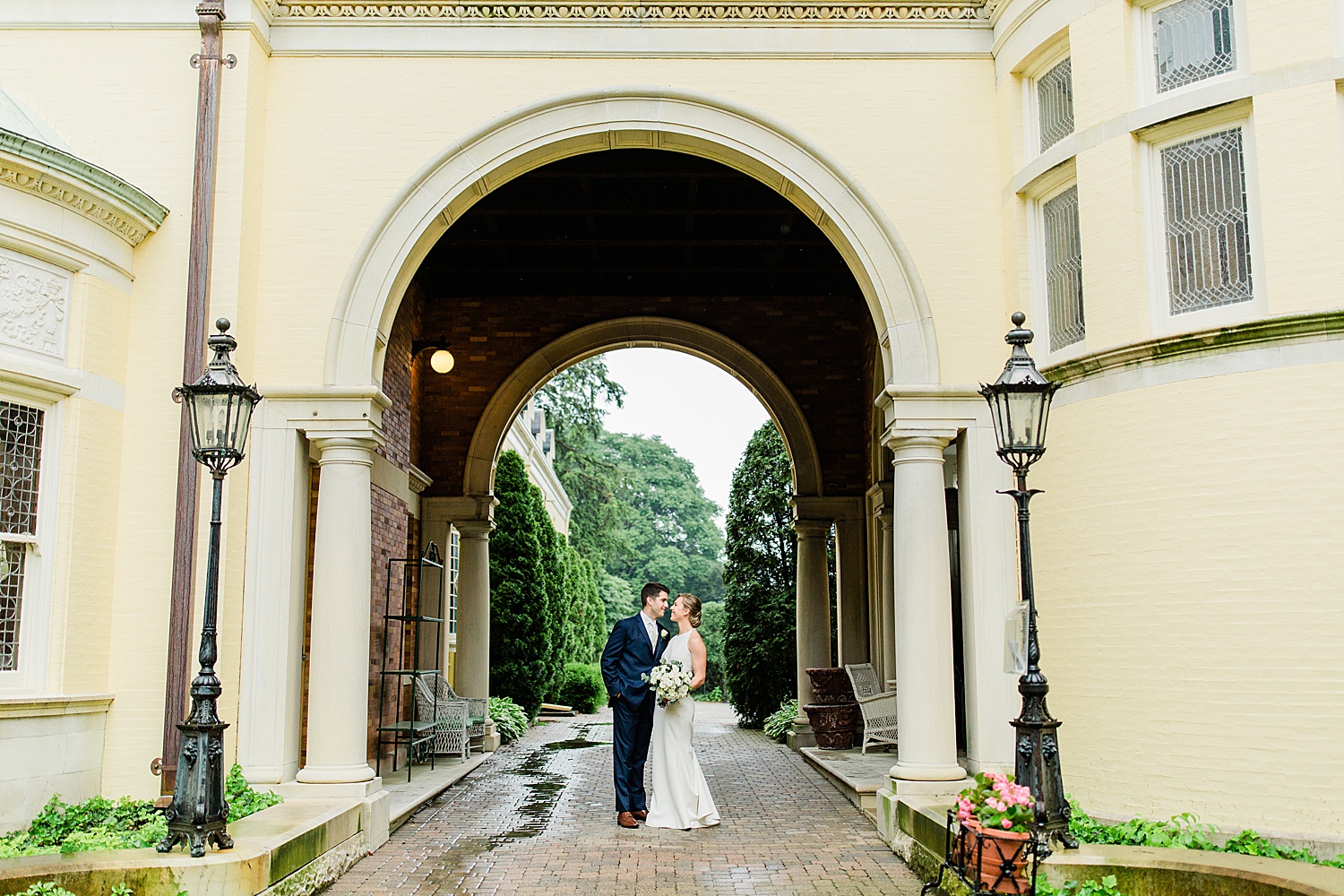 couple stand under arch of historic yellow house by Baltimore wedding photographer 
