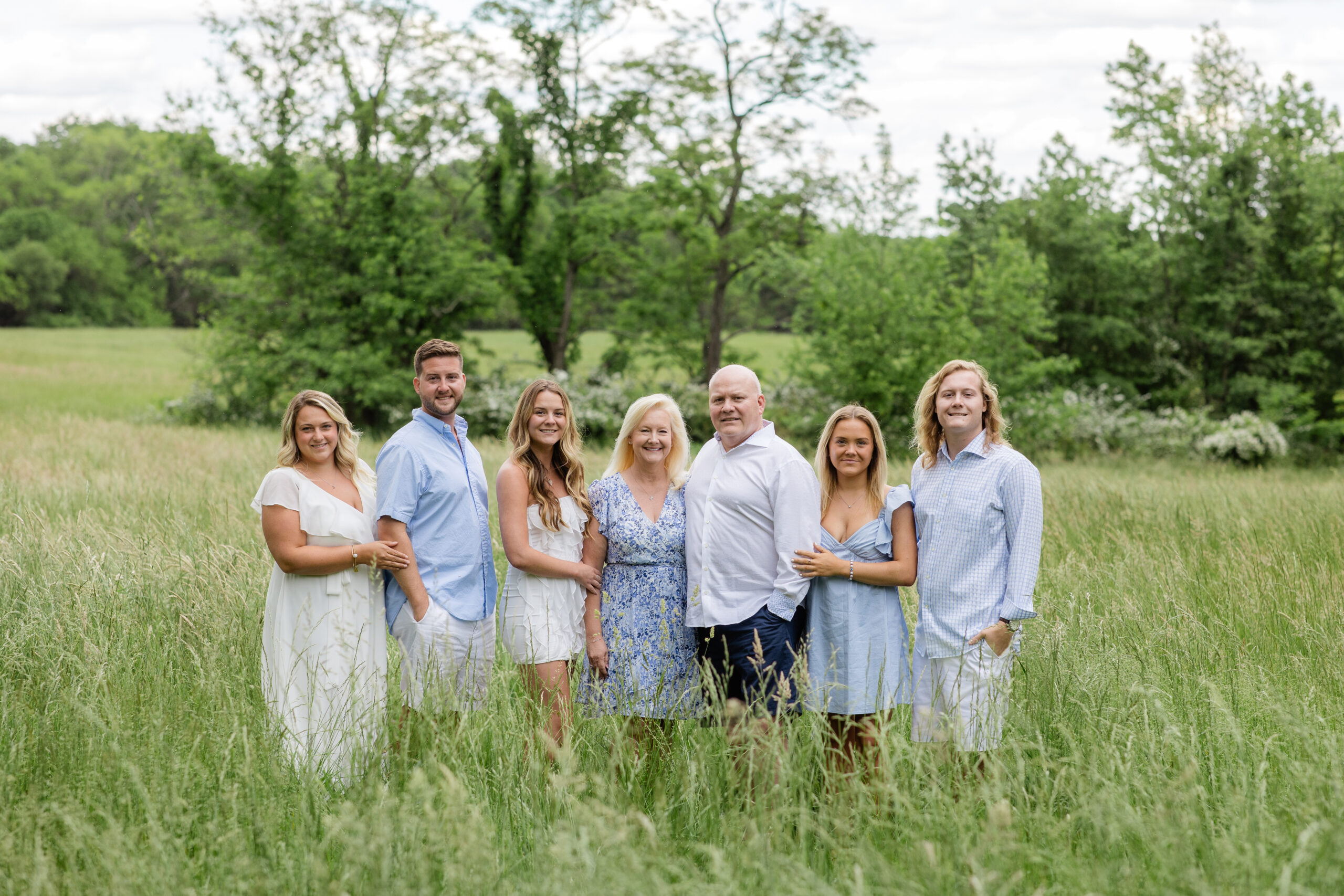 family photoshoot outfits ideas with soft blue and neutral tones for a multi generation family portrait in a green field