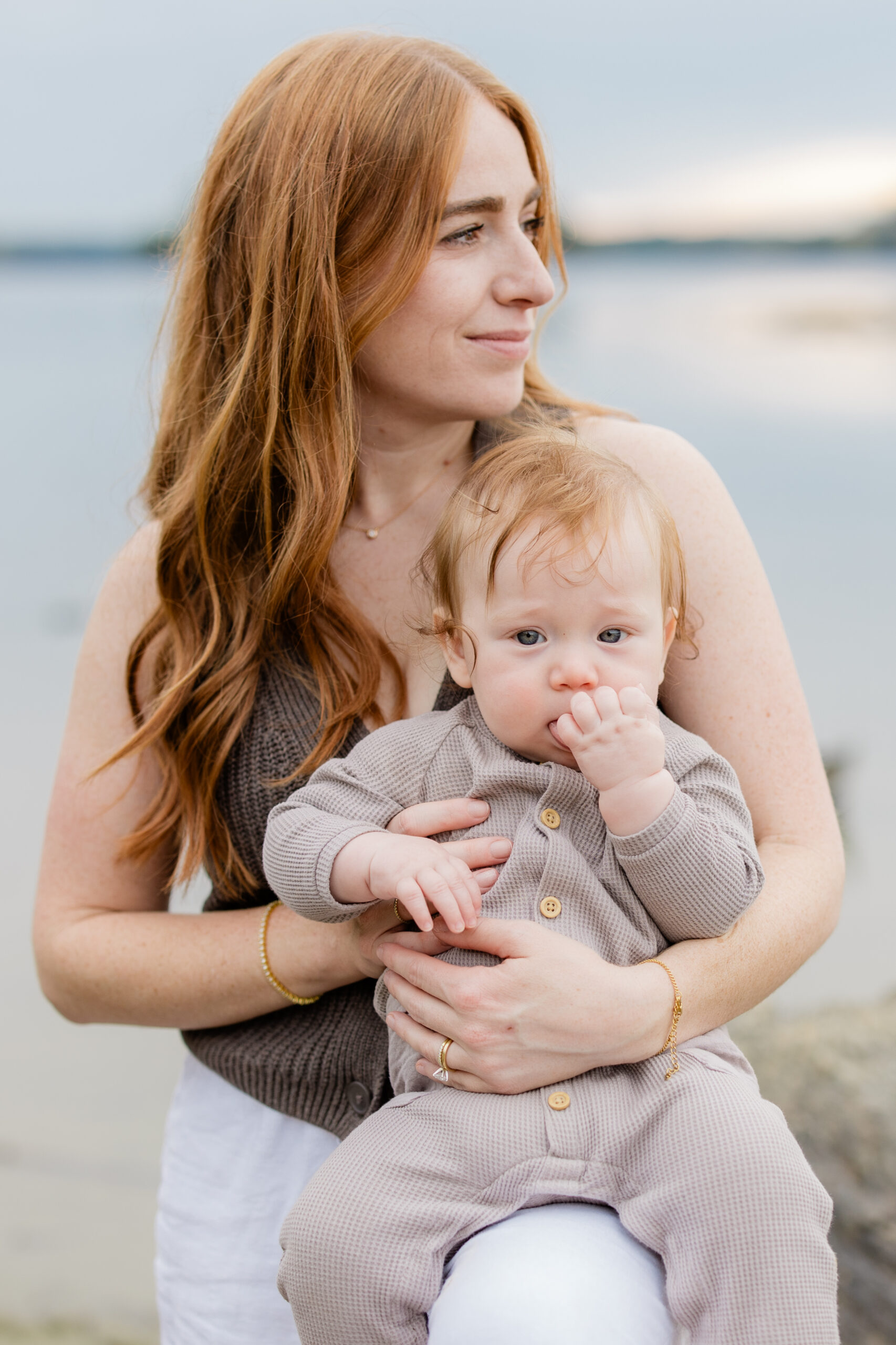 mother holding baby during a lifestyle family photoshoot with neutral outfits by the water