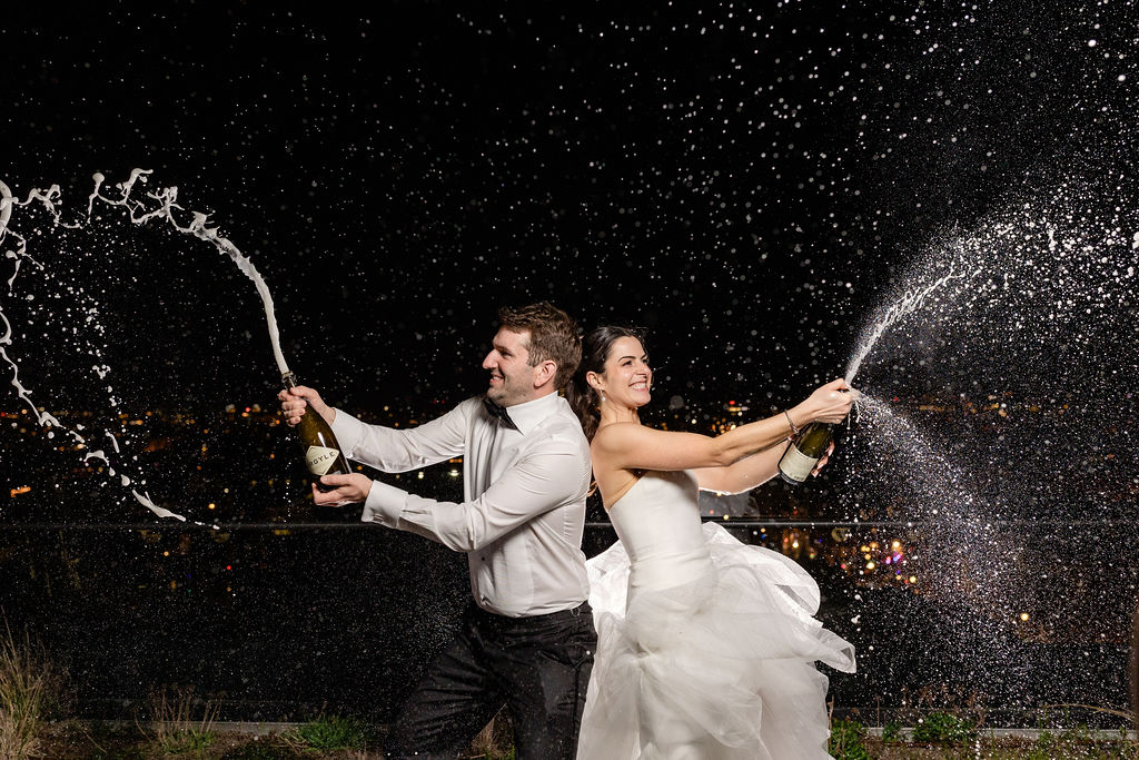 bride and groom popping champagne at night during their wedding celebration overlooking washington dc