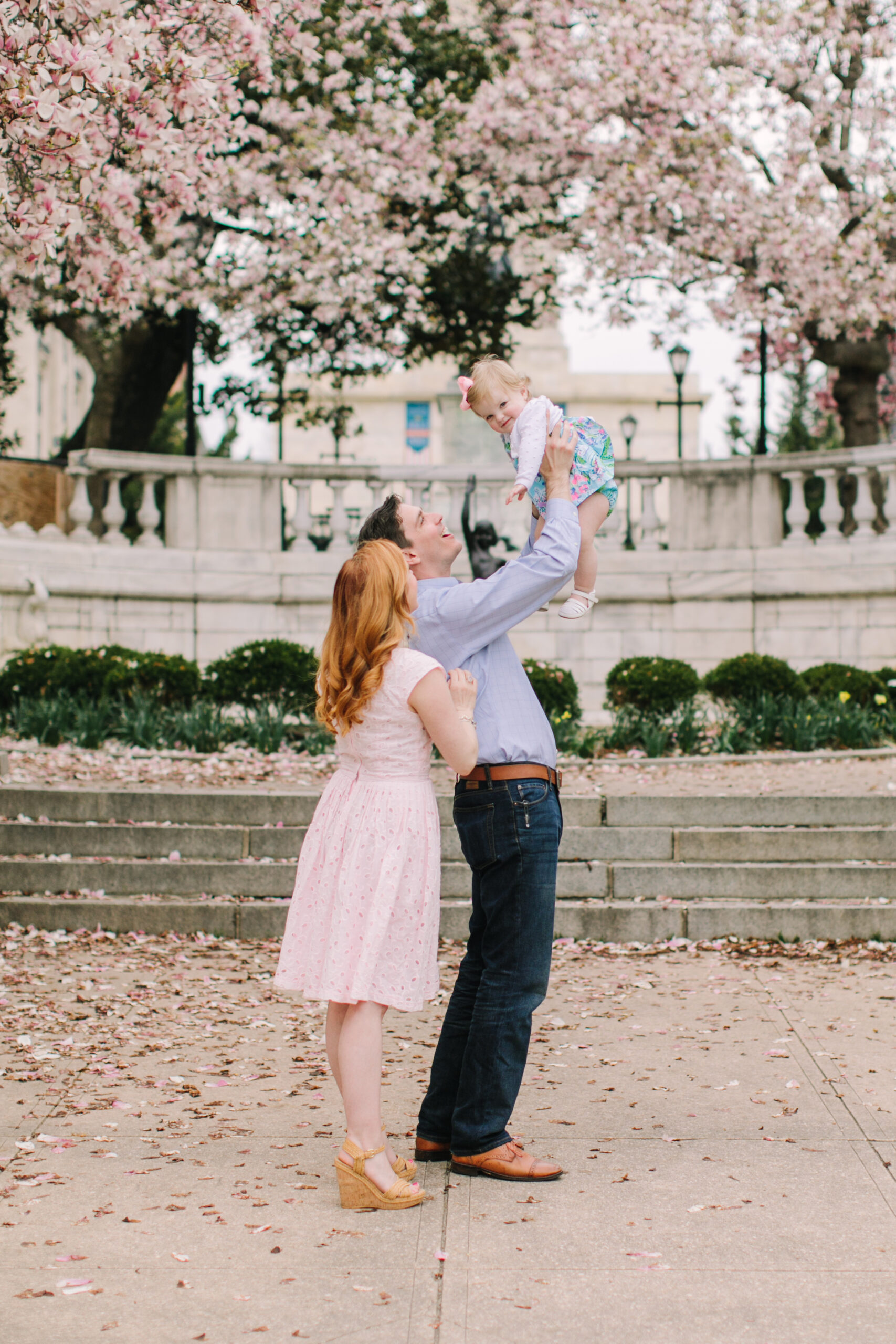 A mom and dad smiling at their daughter during a spring photoshoot 