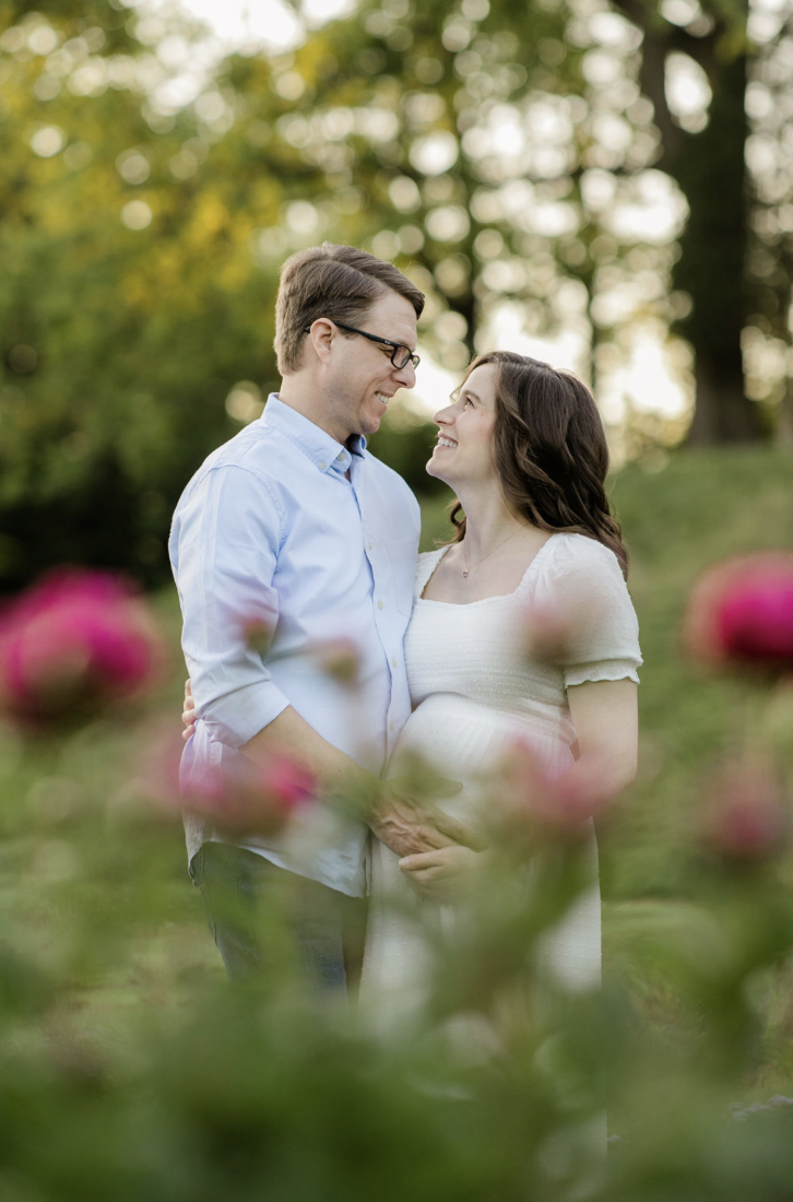expecting parents smiling together surrounded by soft greenery
