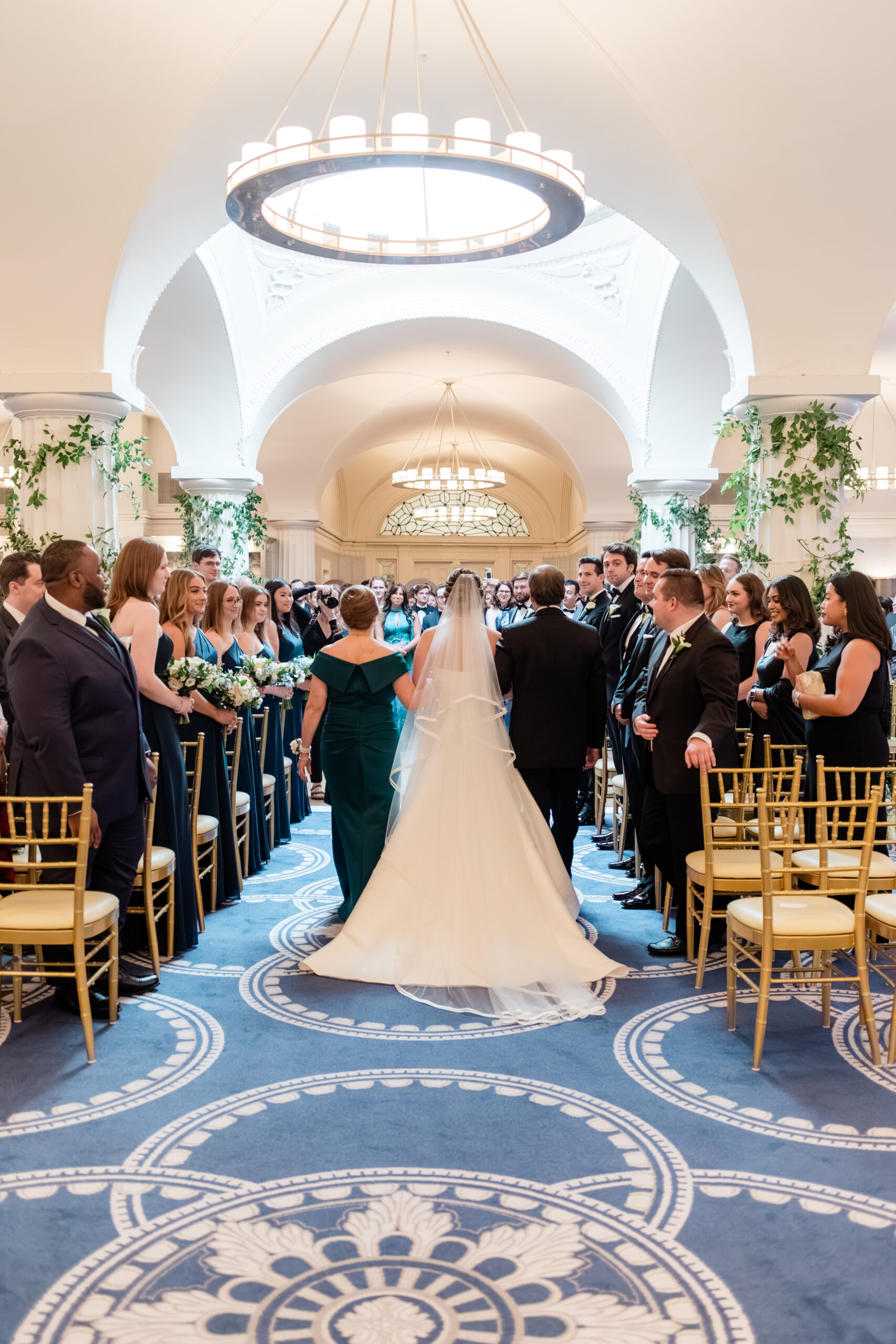 bride walking down aisle during indoor wedding ceremony with guests seated