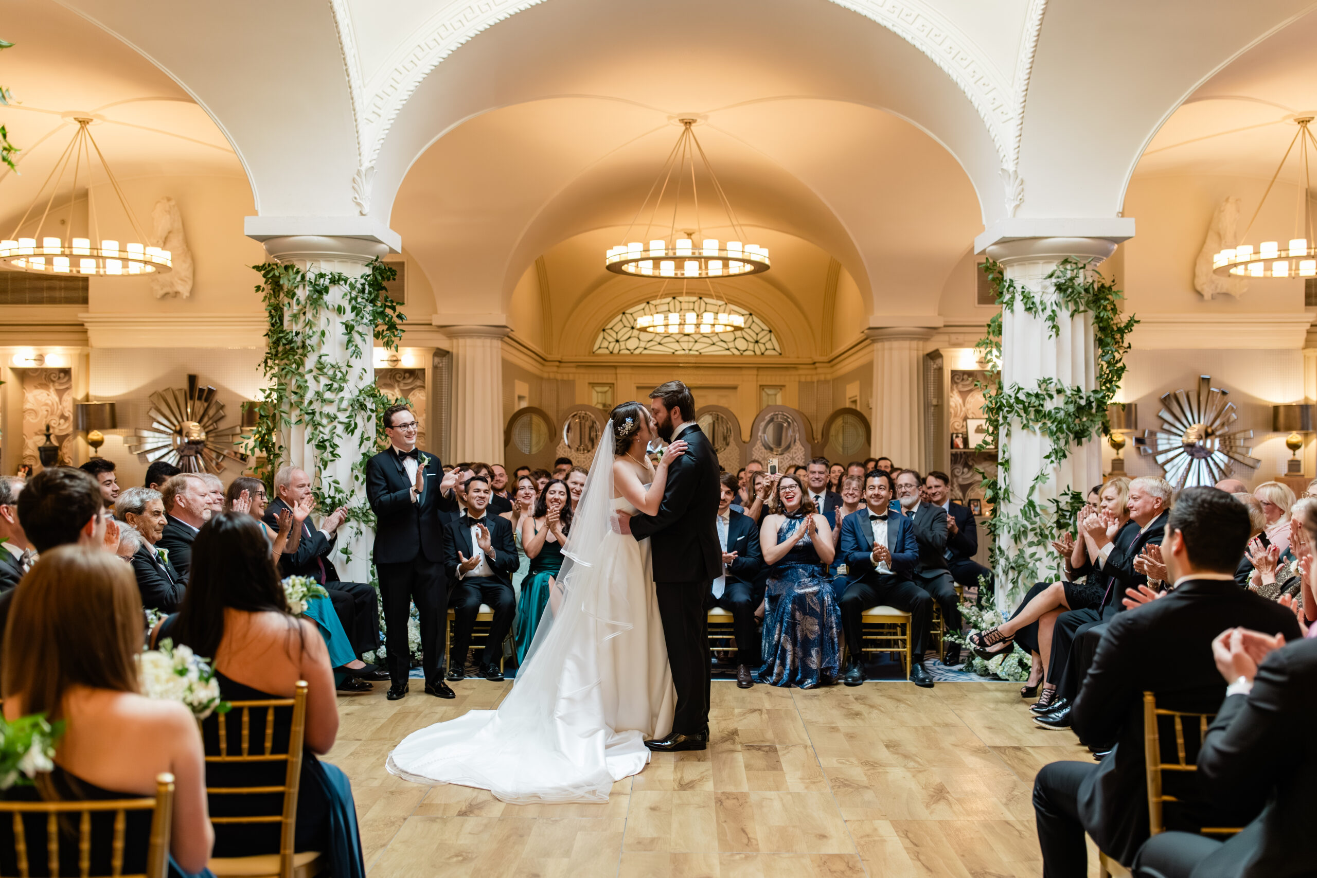couple sharing first kiss during indoor wedding ceremony surrounded by guests