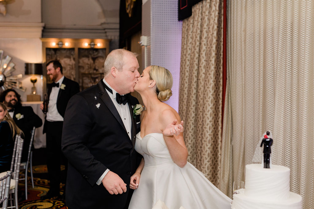 bride and groom sharing a kiss while cutting cake at wedding reception