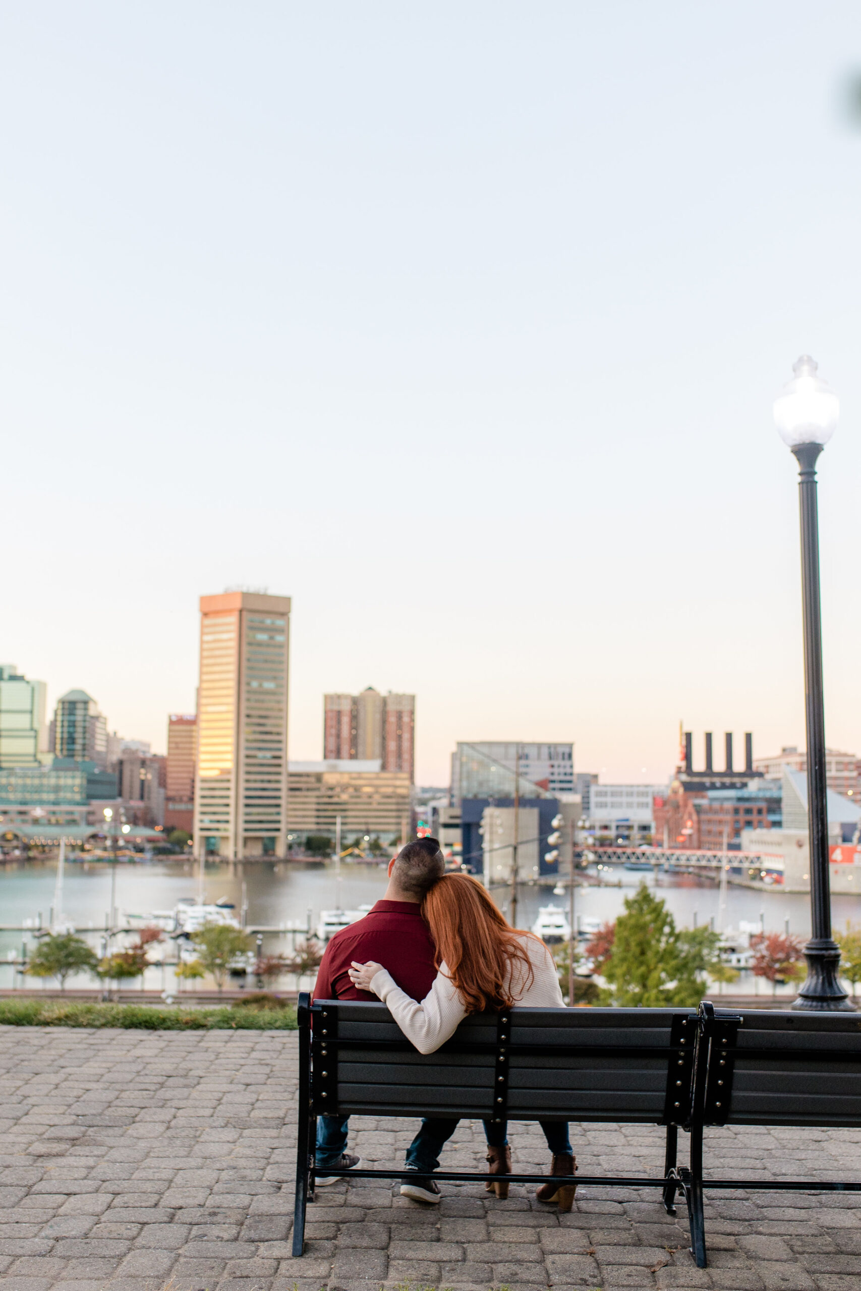 Romantic bench portrait overlooking the Baltimore skyline at sunset during an engagement session in Federal Hill