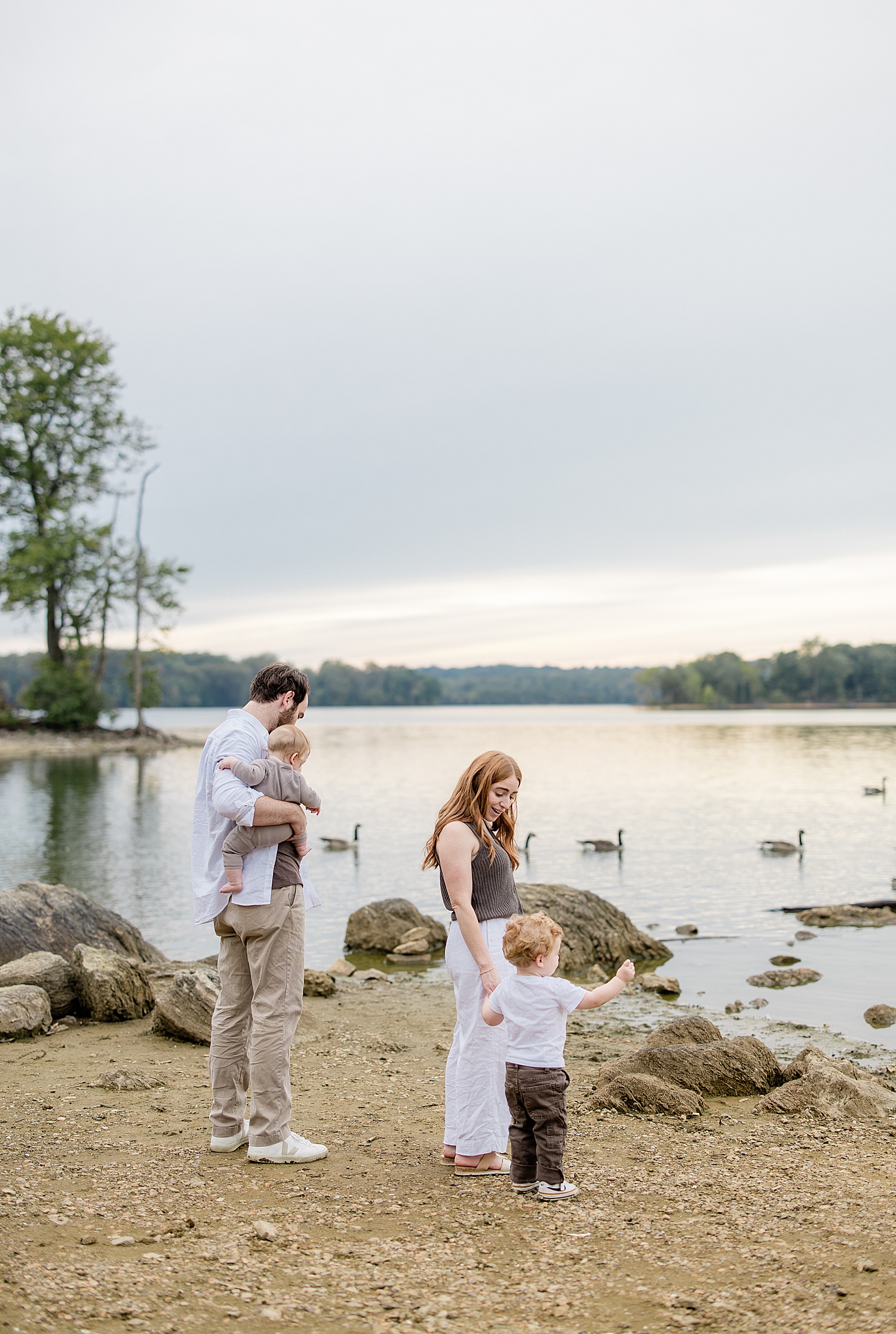 family of four stands on lakefront together by Jen Harvey Photography