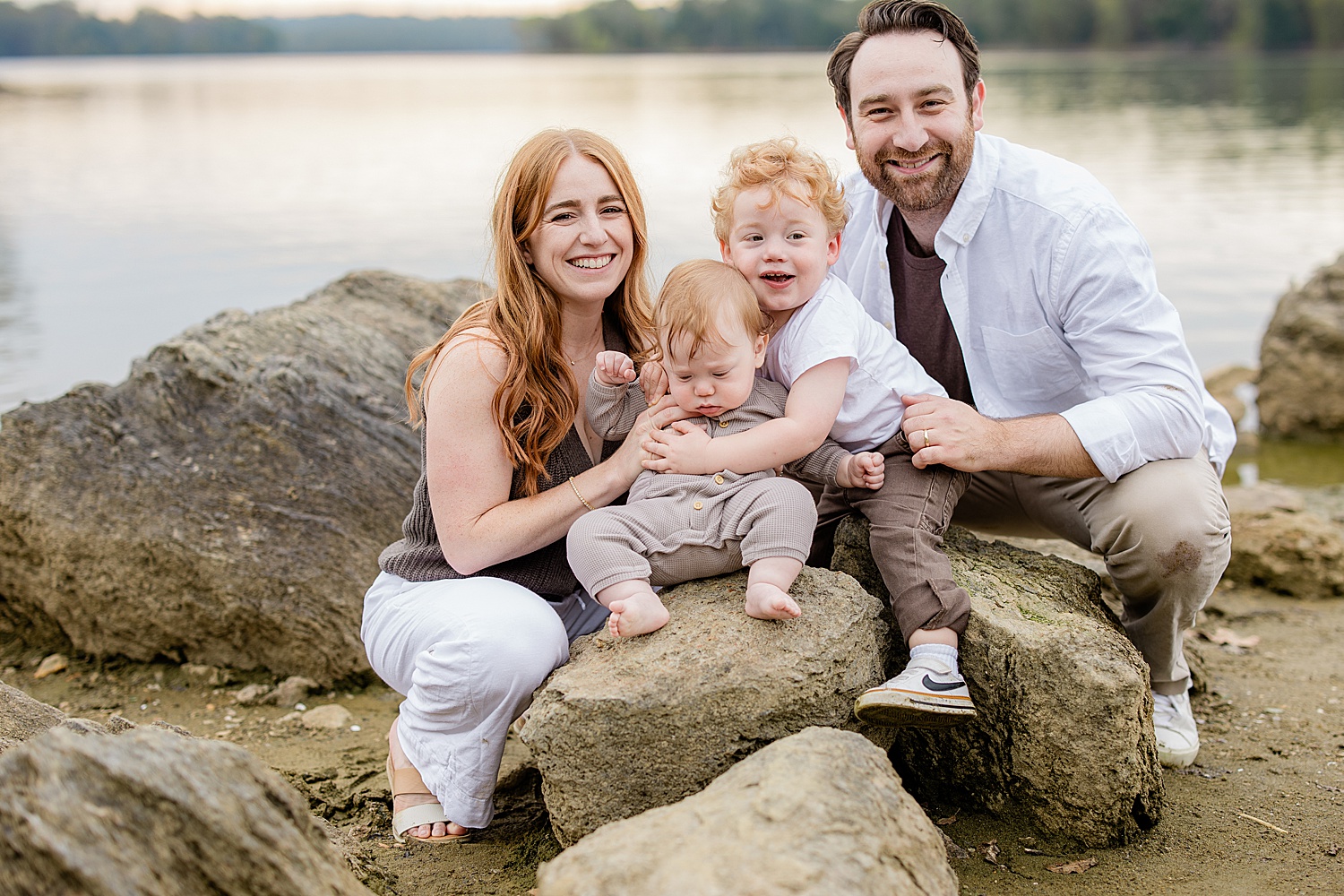 husband and wife snuggle their kids on rocks in Sherwood Garden documenting young families