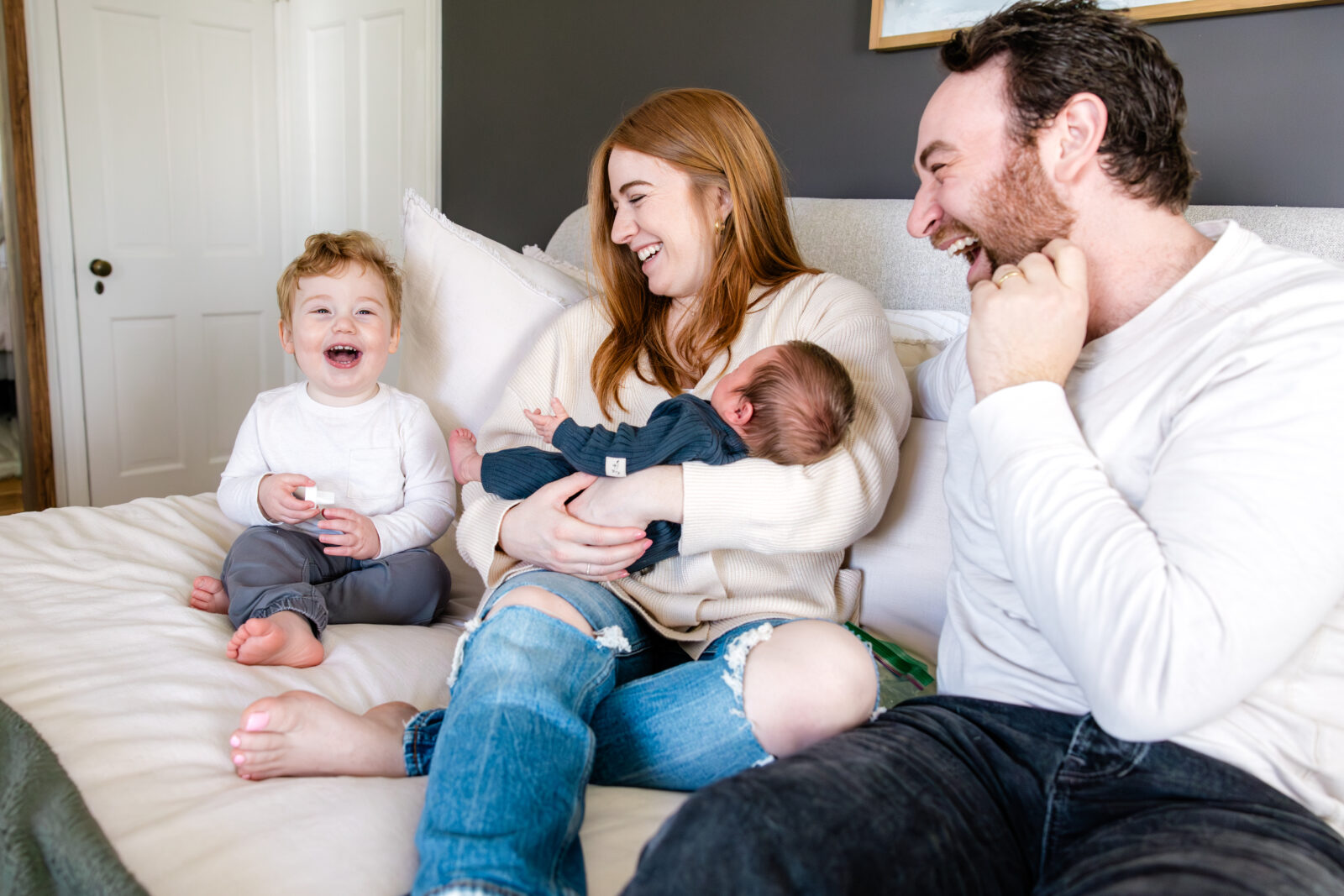 A family of four laughing on the bed.