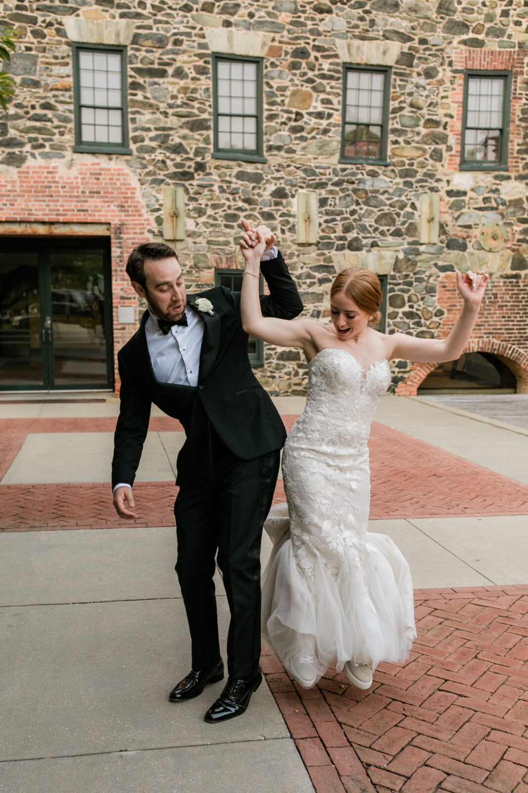 A bride and groom dancing in front of a stone building.