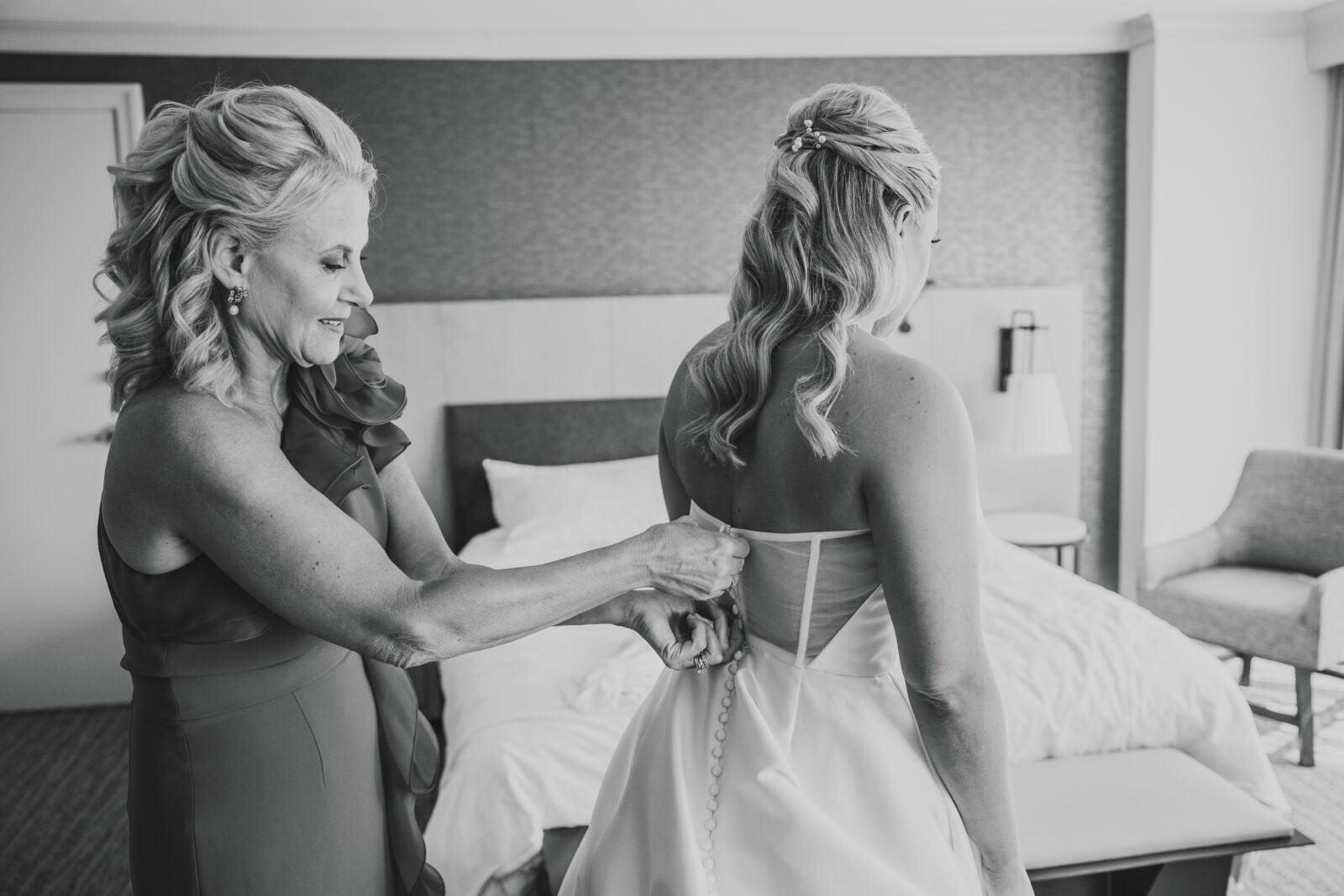 black and white photograph of bridesmaid helping bride zip up her wedding dress