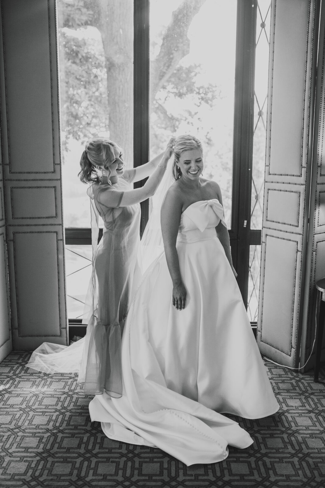 black and white photograph of bridesmaid helping bride with her veil