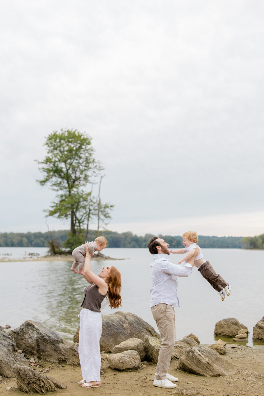 A couple holds their newborn and toddler aged sons in the air during a photo session with a Baltimore family photographer.