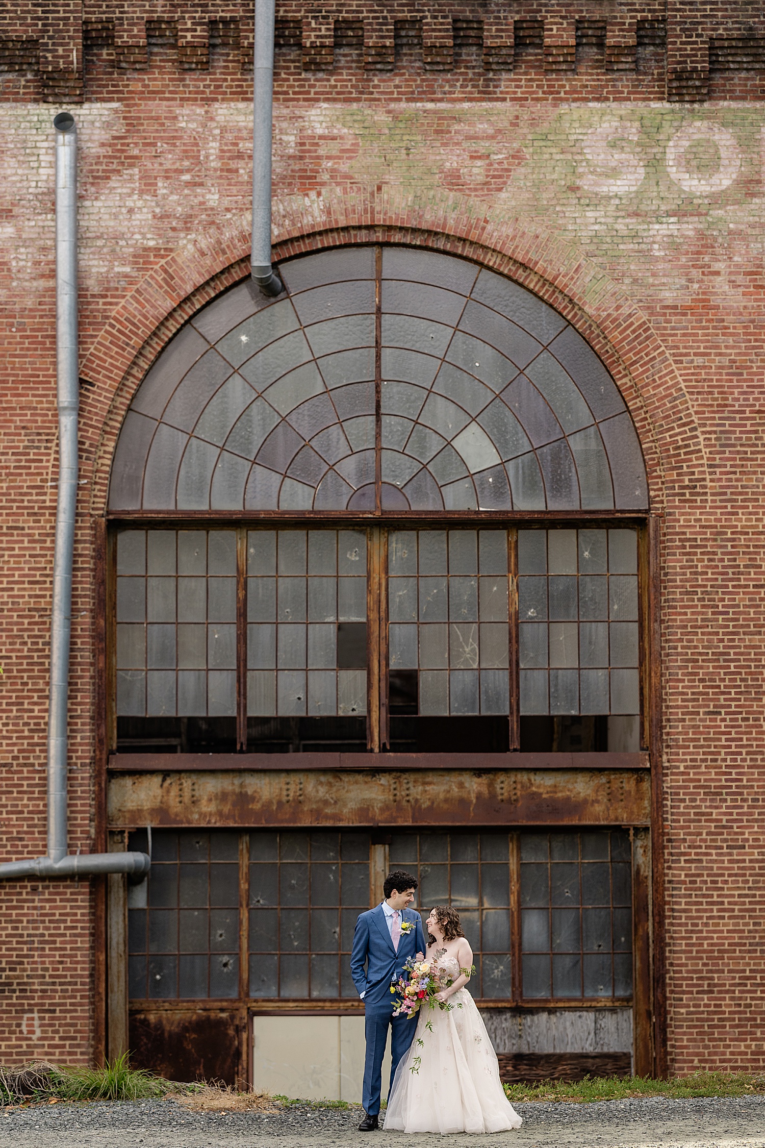 newlyweds stand in front of old arch window by Baltimore wedding photographer