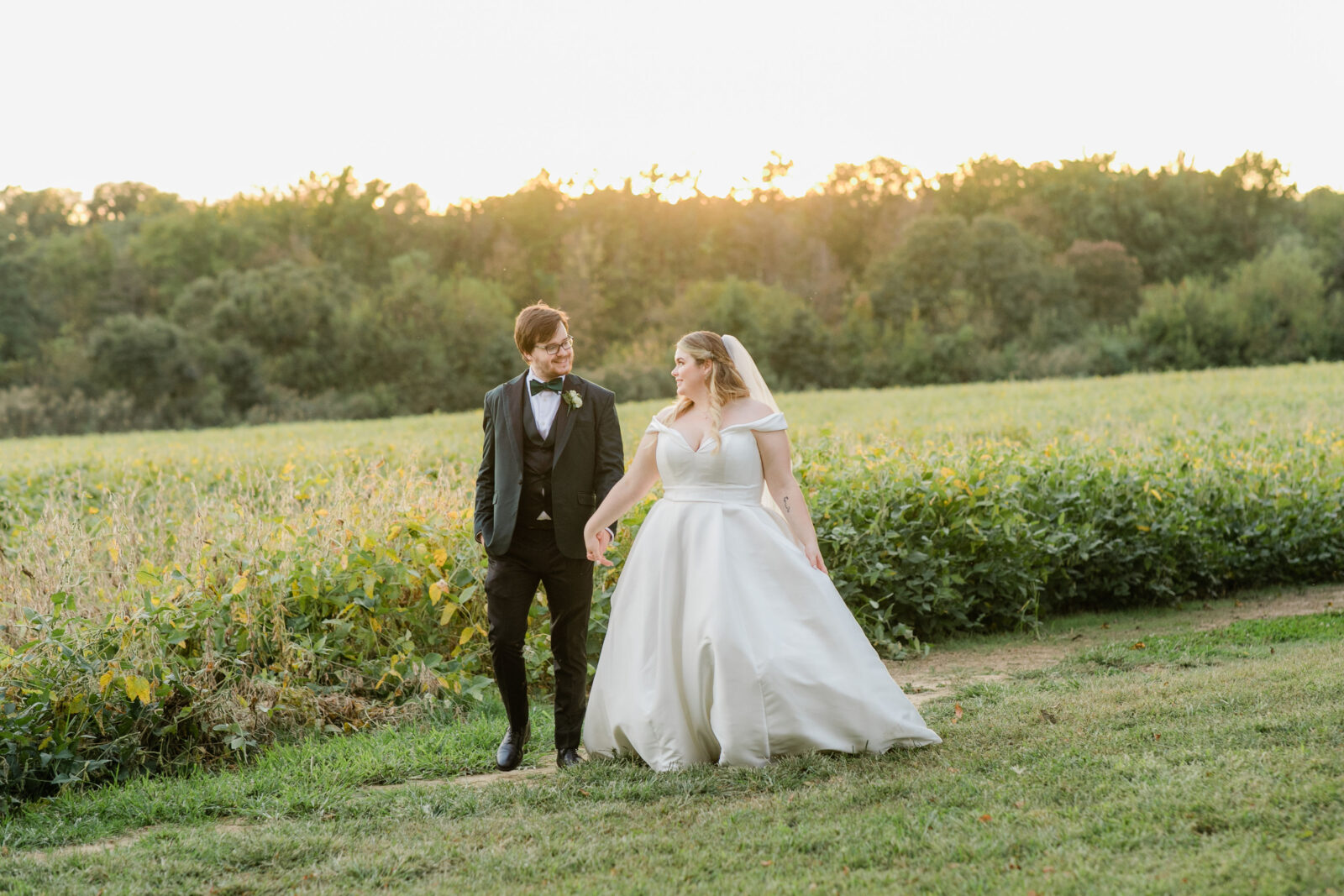 Bride and groom walking in fields with the sun setting