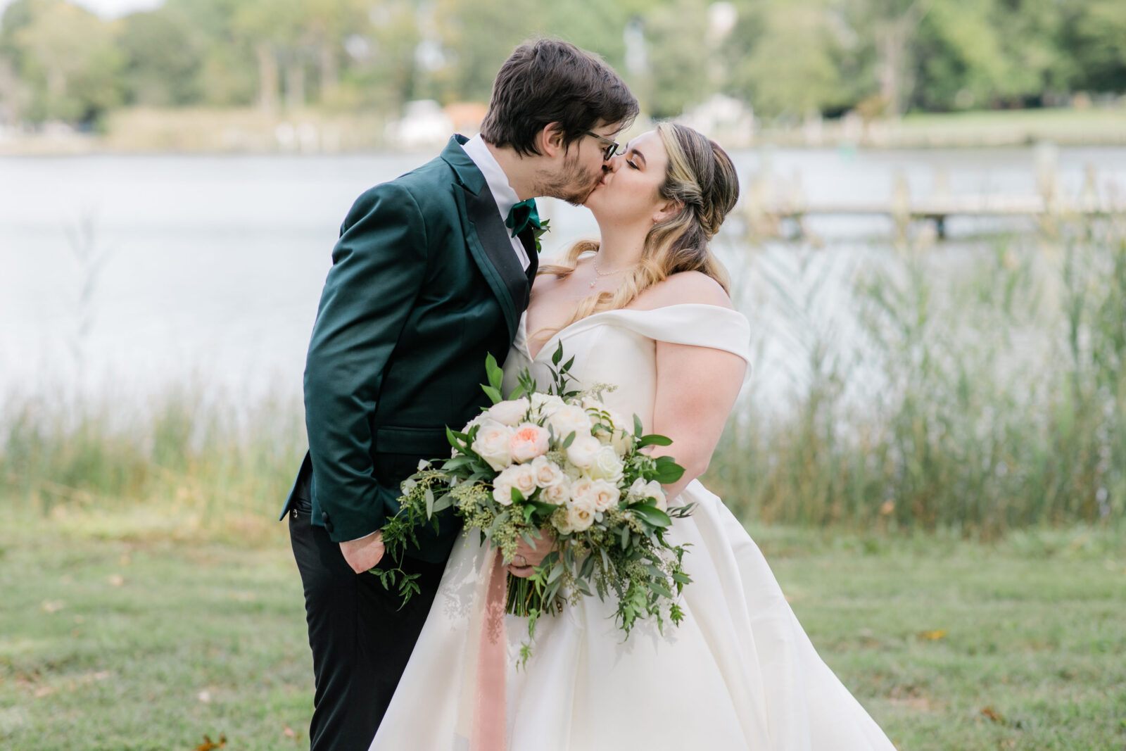 Bride and groom sharing a kiss in front of water on the grounds of Kent Island Resort
