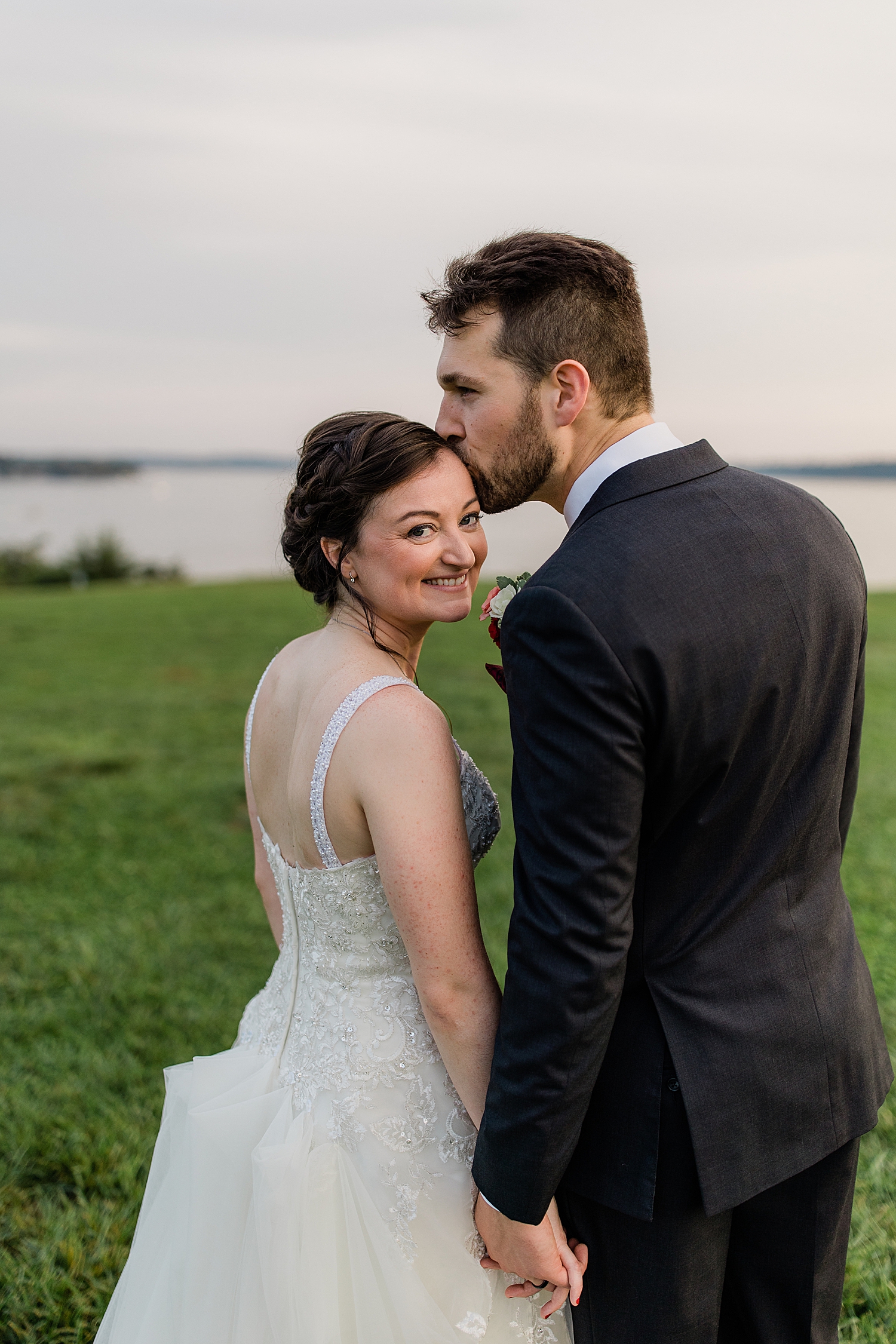 man leans in to kiss woman's temple by a lake by Jen Harvey Photography