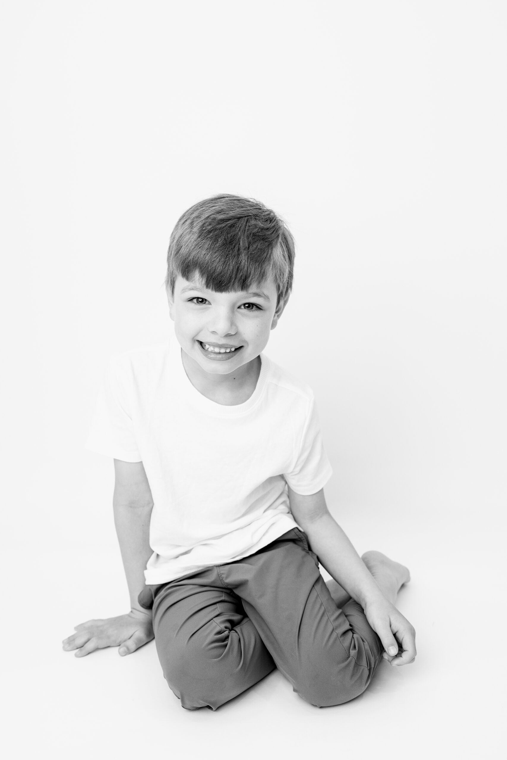 Black and white portrait of young boy kneeling on studio floor with a gentle smile