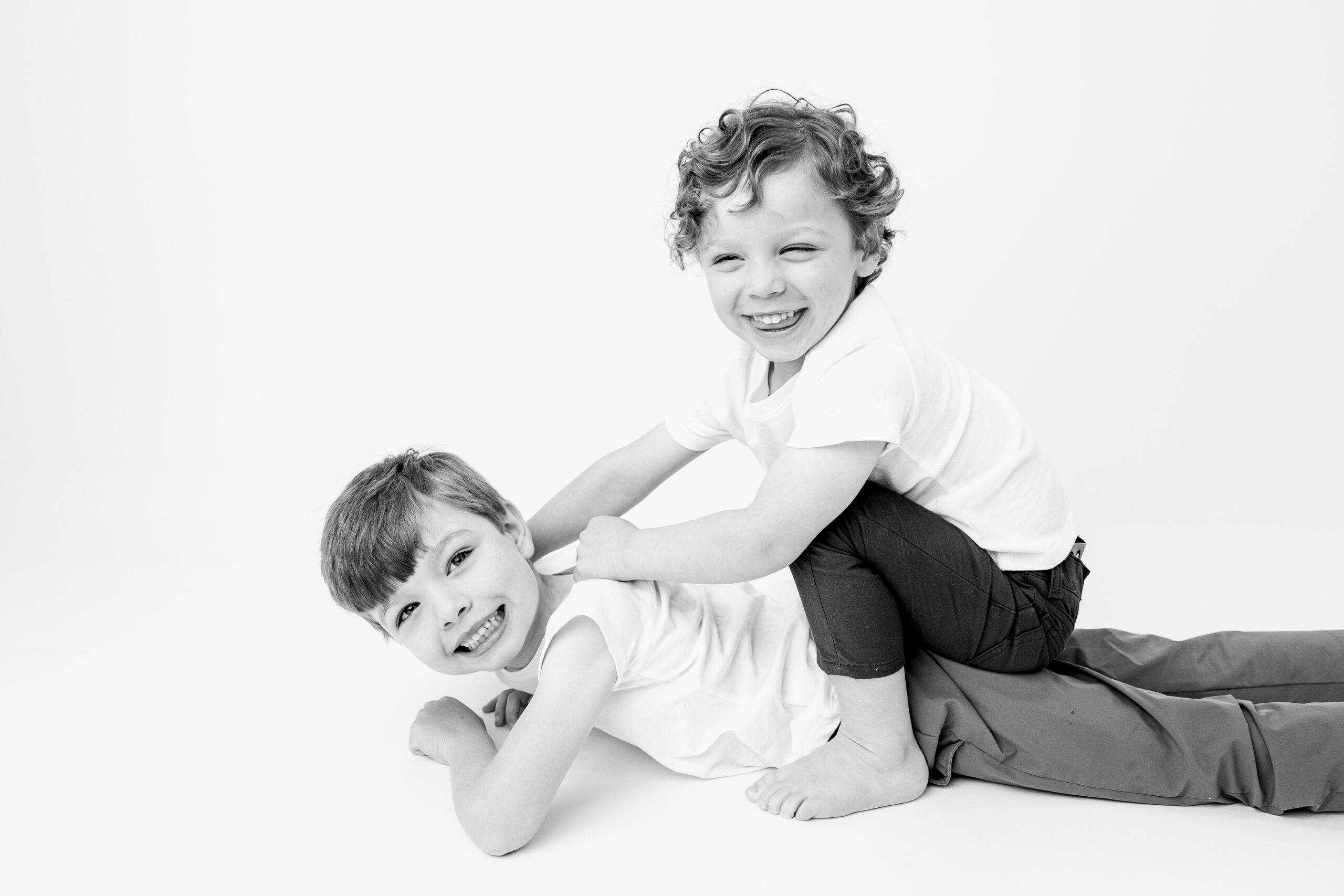Brothers playfully wrestling on the studio floor, one boy grinning straight at the camera