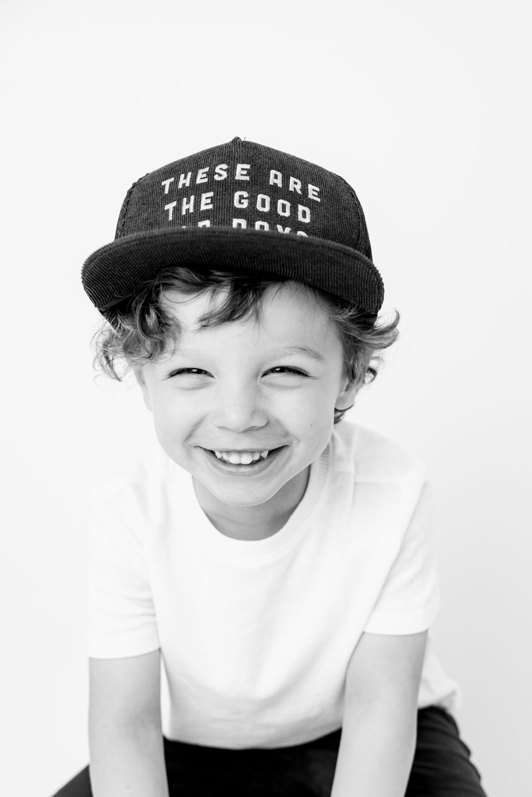 Curly haired boy in a hat smiling child photographer Baltimore studio portrait
