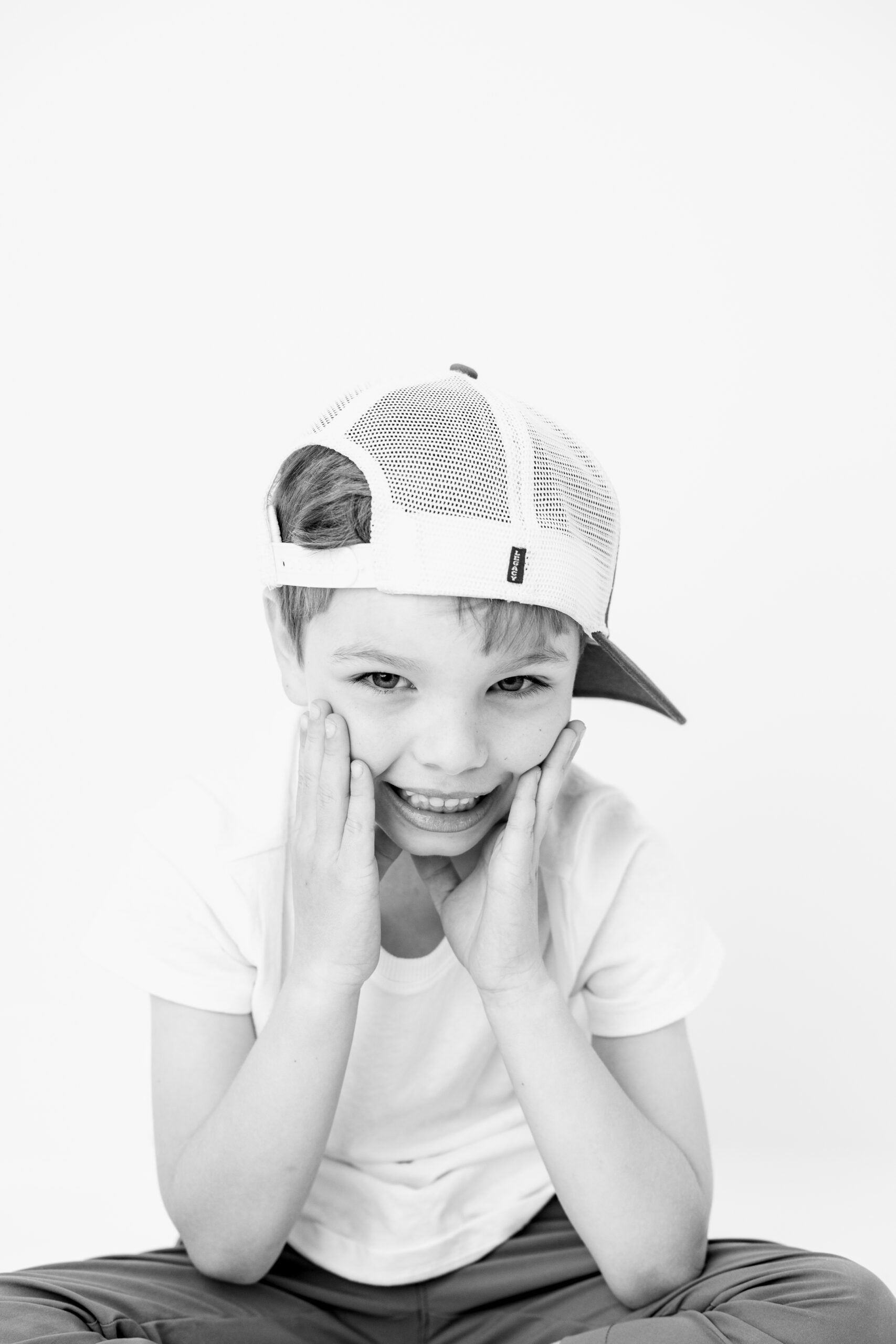 Boy wearing a backwards cap with hands on his cheeks, child photographer Baltimore portrait