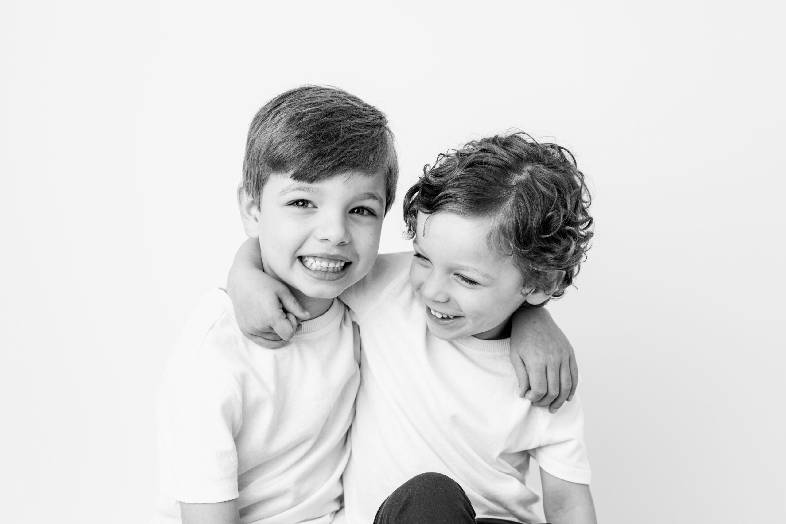 Baltimore children's photographer captures two brothers laughing with arms around each other in a black and white portrait