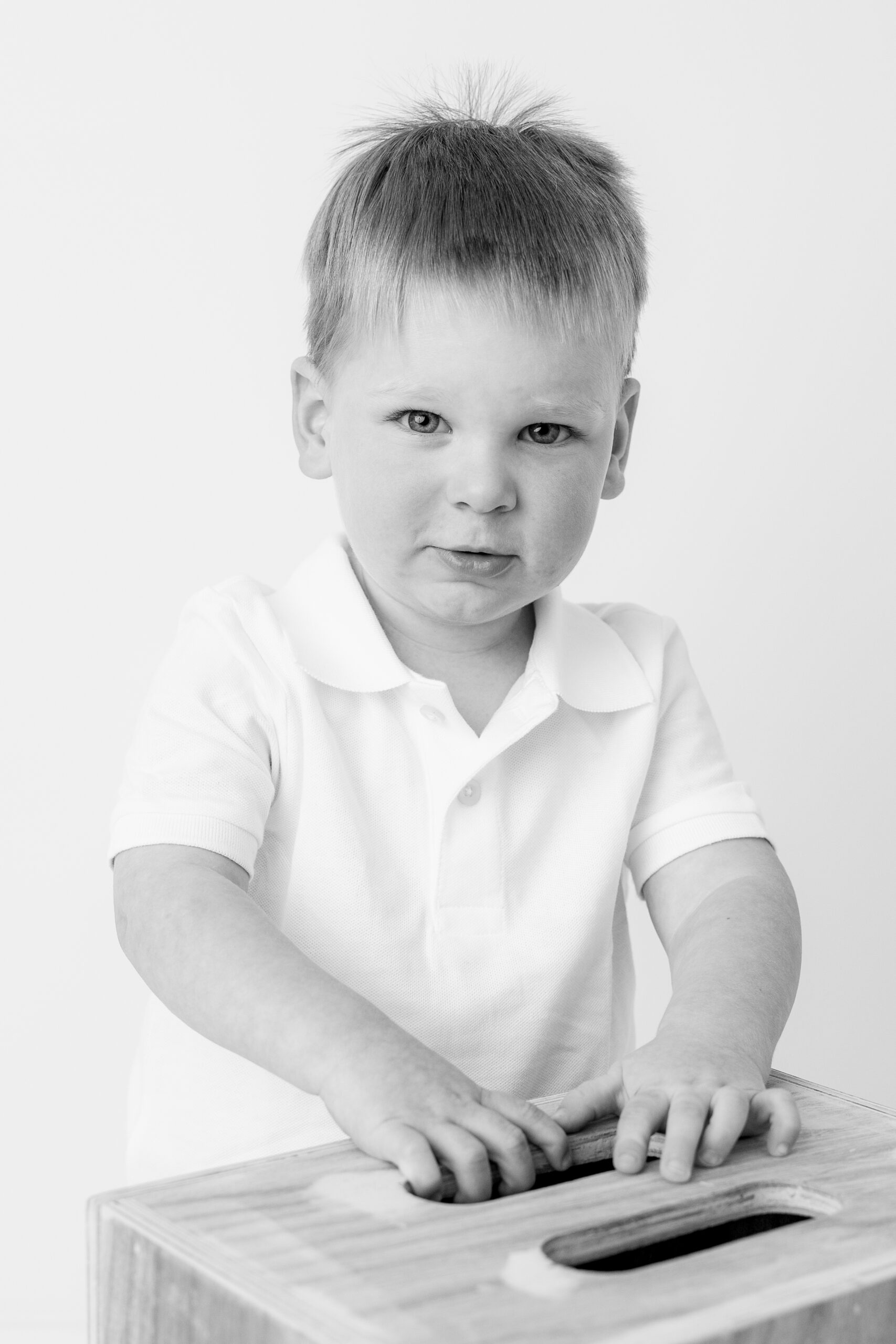 Black and white image of a toddler boy playing next to a wood box