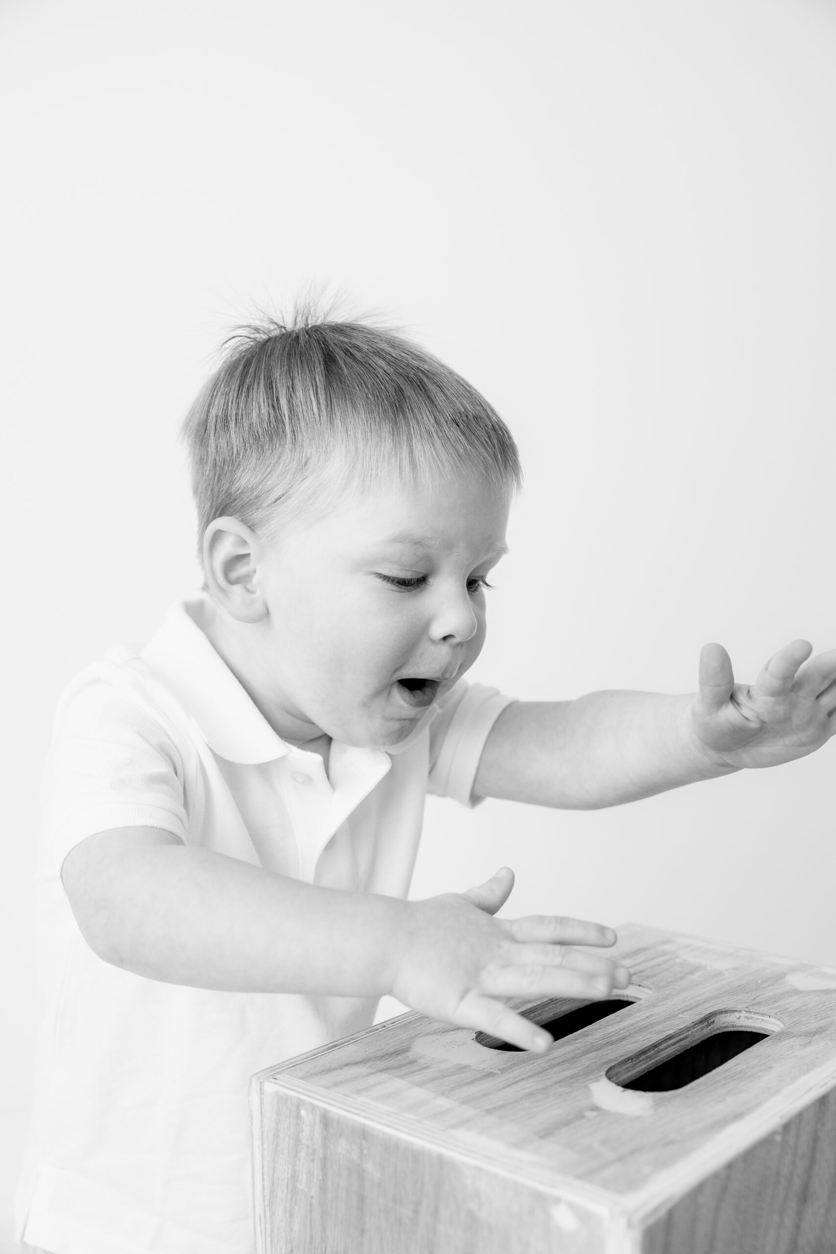 Black and white image of a toddler boy playing next to a wood box