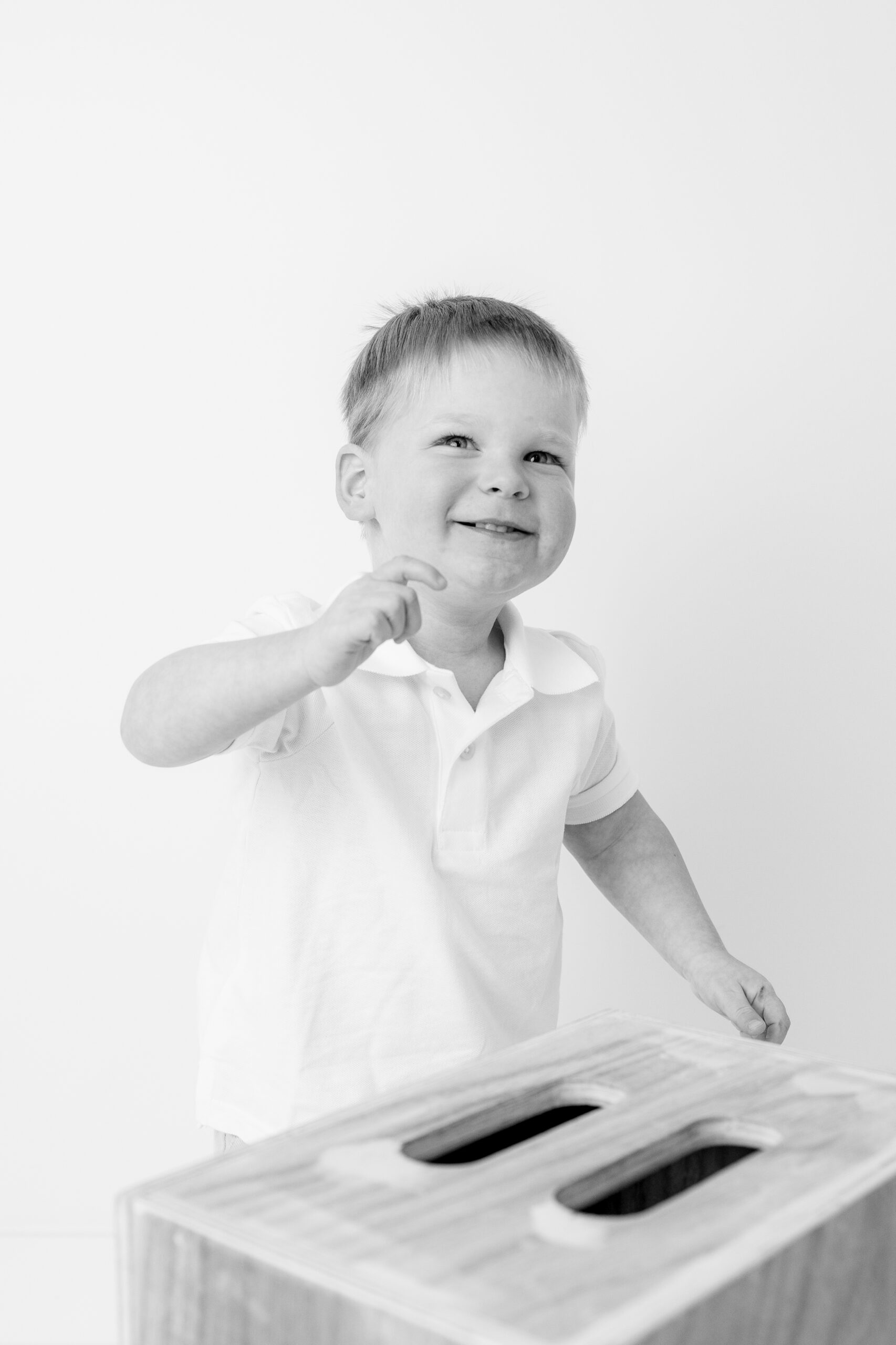 Black and white image of a toddler boy playing next to a wood box